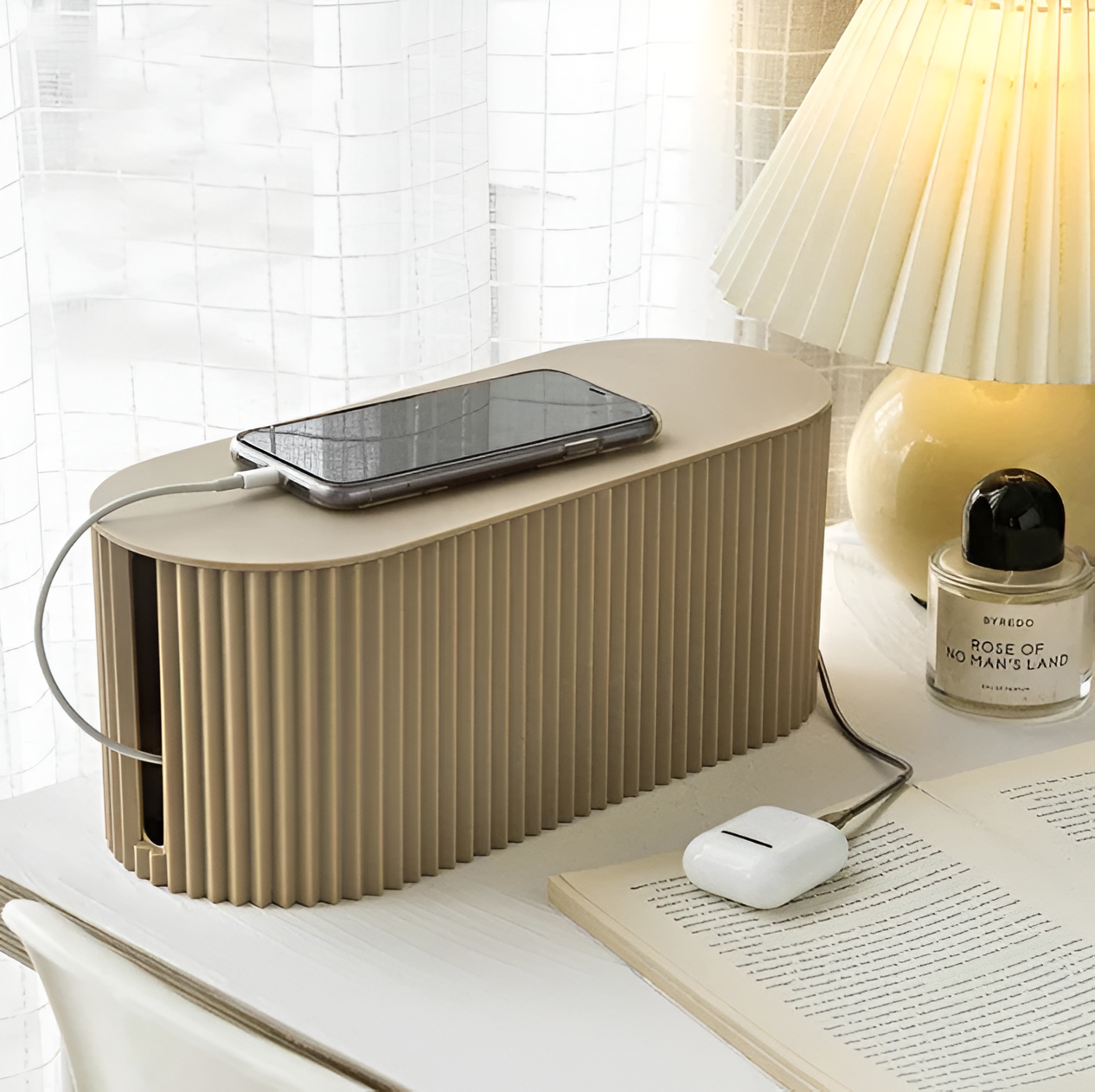 Beige ribbed cable organizer box on a desk with a charging phone and AirPods, creating a minimalist home setup.
