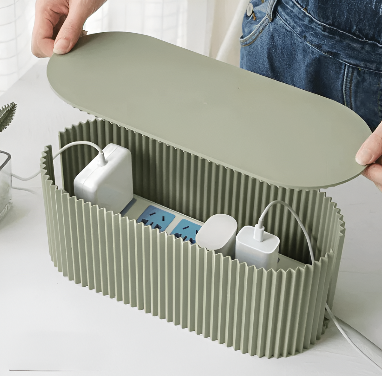 Fitlybuy soft green, oval-ribbed cable organizer box holding a power strip with white chargers on a white table.