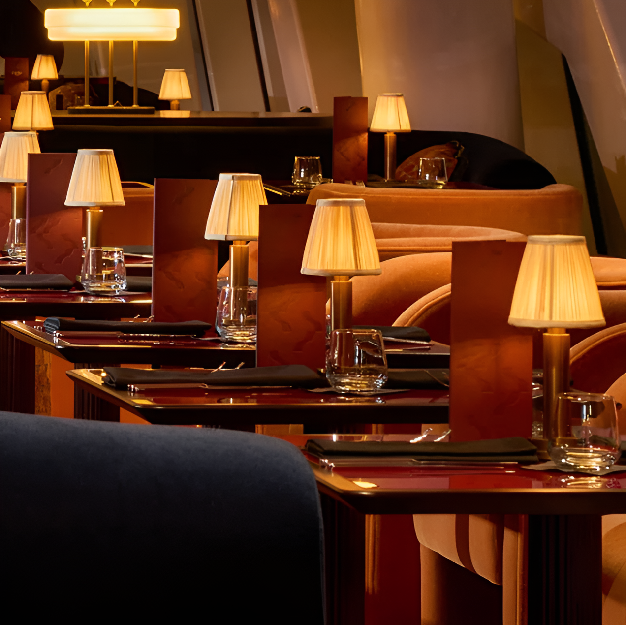 Vintage dimmable aluminium table lamps with fabric shades illuminate restaurant tables, creating a warm, moody atmosphere.