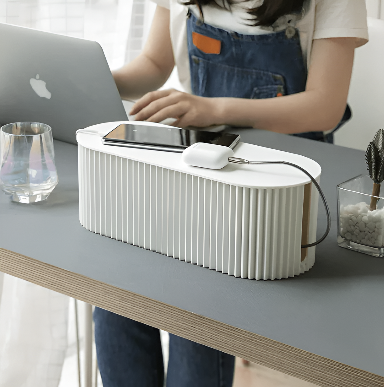 Fitlybuy white, oval, ribbed cable organizer box on a desk, holding a smartphone and charging earbuds.