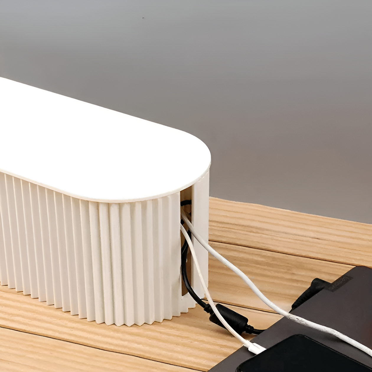 Minimalist white Fitlybuy cable organizer box with a ribbed texture, sitting on a wooden desk with charging cables.