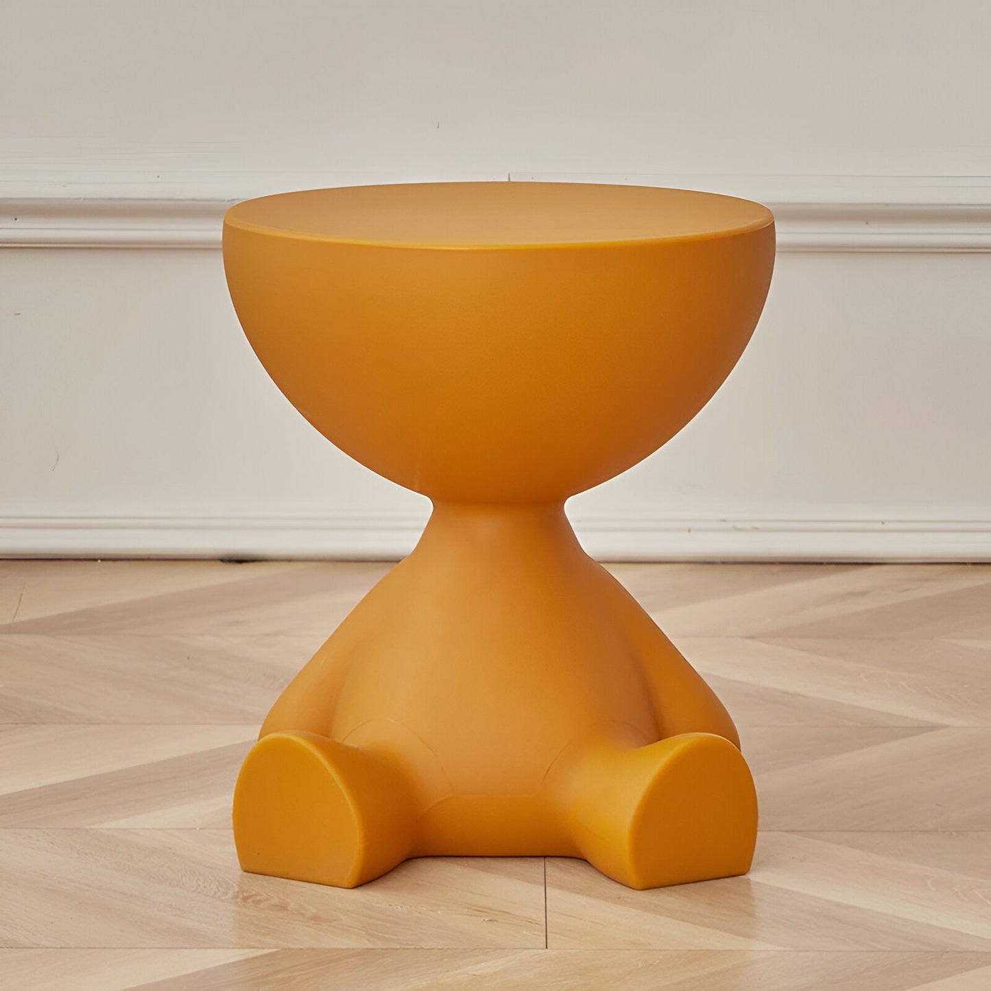 Mustard yellow, whimsical round coffee table shaped like a seated character, set on a light wood floor.