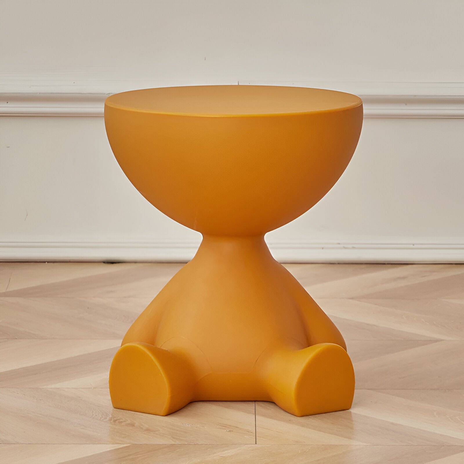 Mustard yellow, whimsical round coffee table shaped like a seated character, set on a light wood floor.