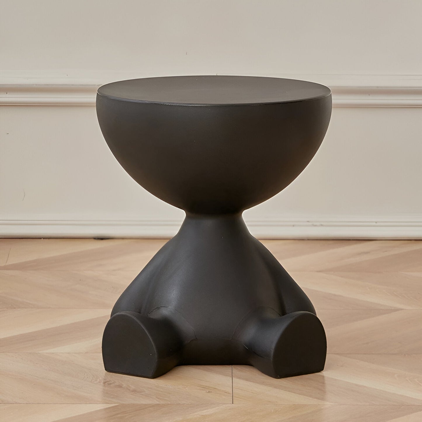 Fitlybuy Ylix matte black, sculptural round coffee table with an artisan, person-shaped base on a hardwood floor.