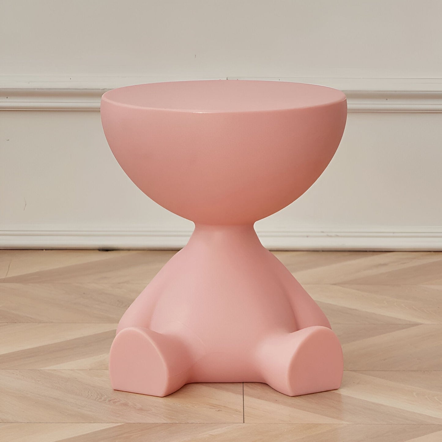 Fitlybuy Ylix round coffee table in pastel pink, shaped like a seated figure, on a light wood floor against a white wall.