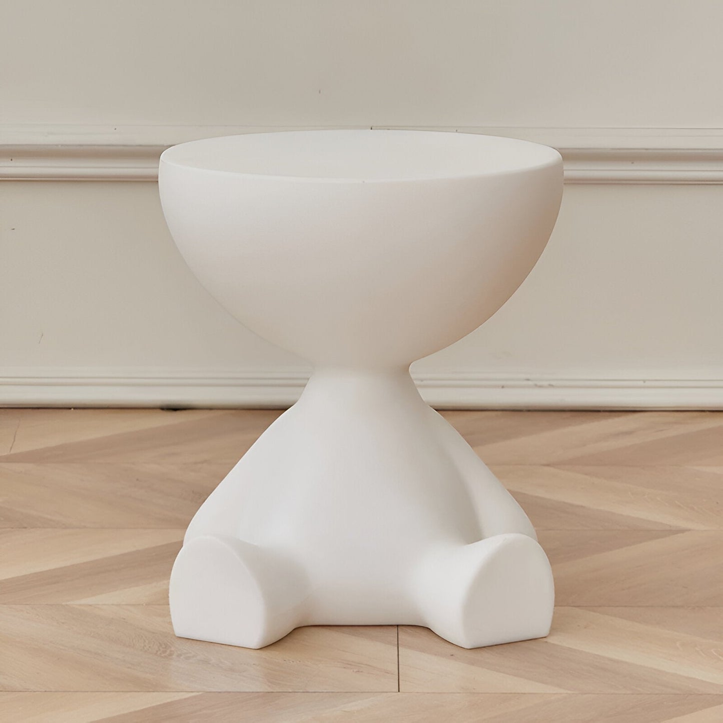 Fitlybuy Ylix matte white round coffee table with a sculptural, seated-figure base on a herringbone wood floor.