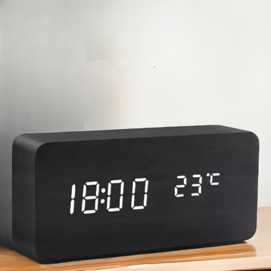 Black wooden rectangular digital alarm clock with white LED display showing time and temperature on a wooden surface.