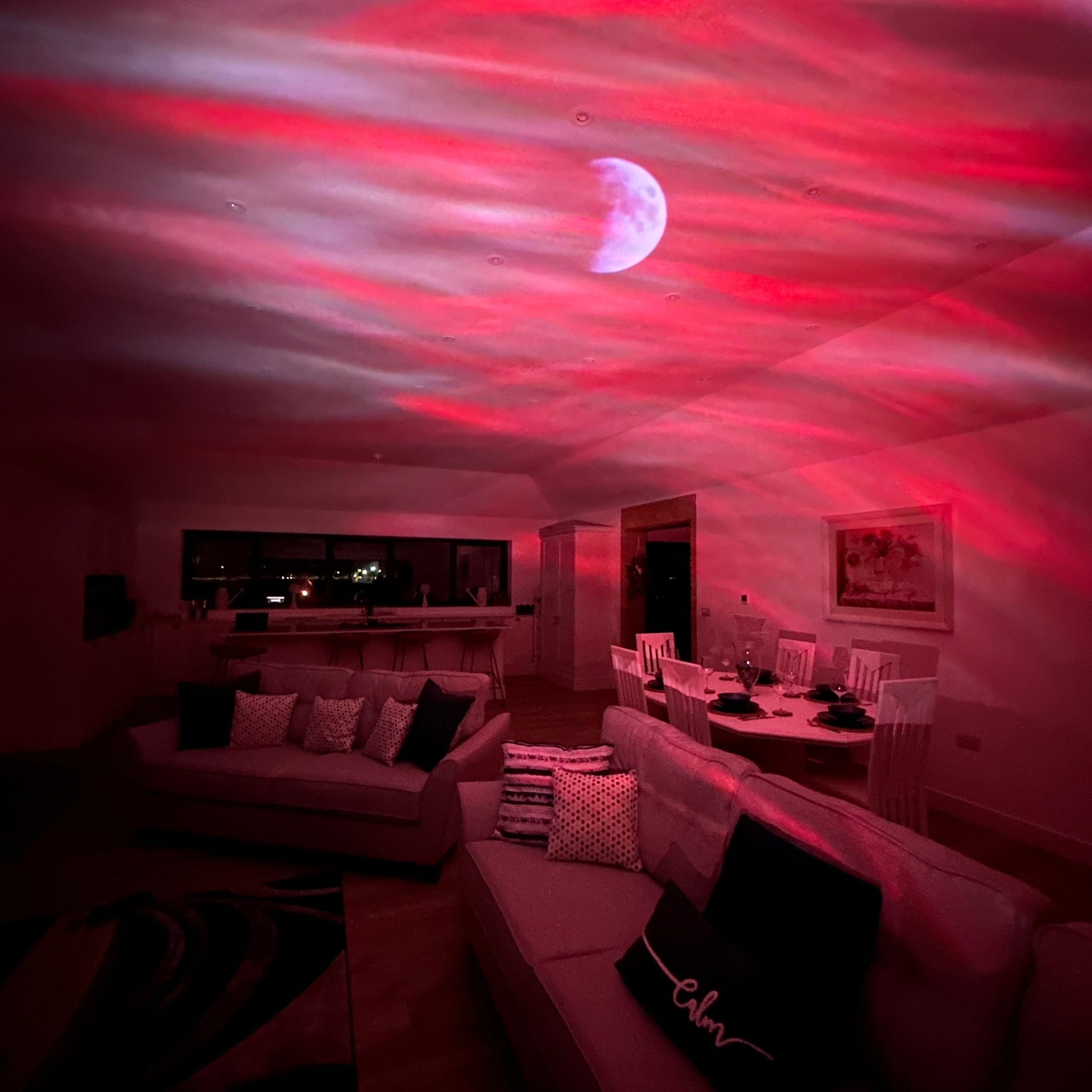 Fitlybuy Aurora projector casts a red, wavy light display and moon onto a living room ceiling for an ambient atmosphere.