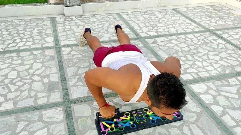 A person does push-ups on a black Fitlybuy multi-functional folding board with color-coded muscle training grips.