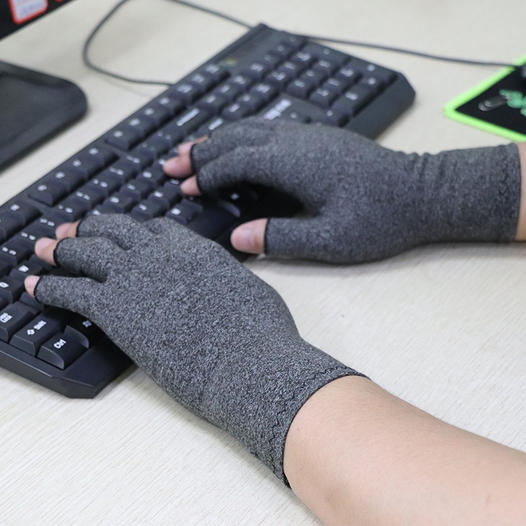 Gray, fingerless Fitlybuy therapeutic compression gloves worn while typing on a computer keyboard.
