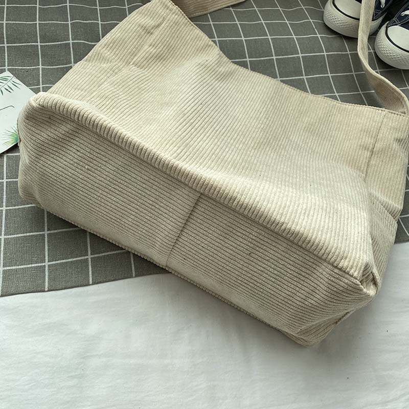 Fitlybuy beige corduroy crossbody bag on a grey grid background with sneakers nearby.