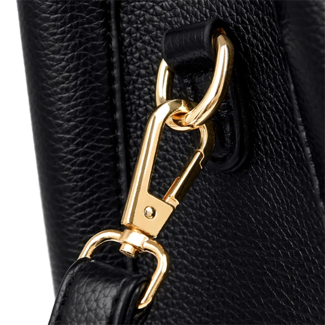 Close-up of black pebble-grain PU leather handbag with a polished gold-tone metal lobster clasp and strap attachment.