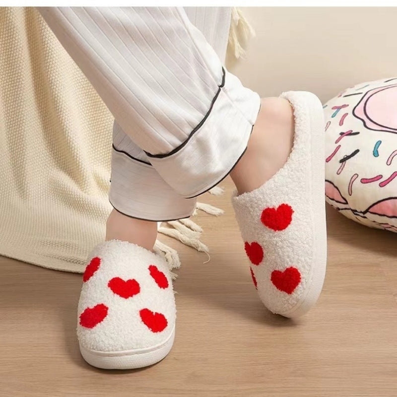 White fuzzy Nordic Comfort slippers with red heart patterns worn with pajamas in a cozy bedroom setting.