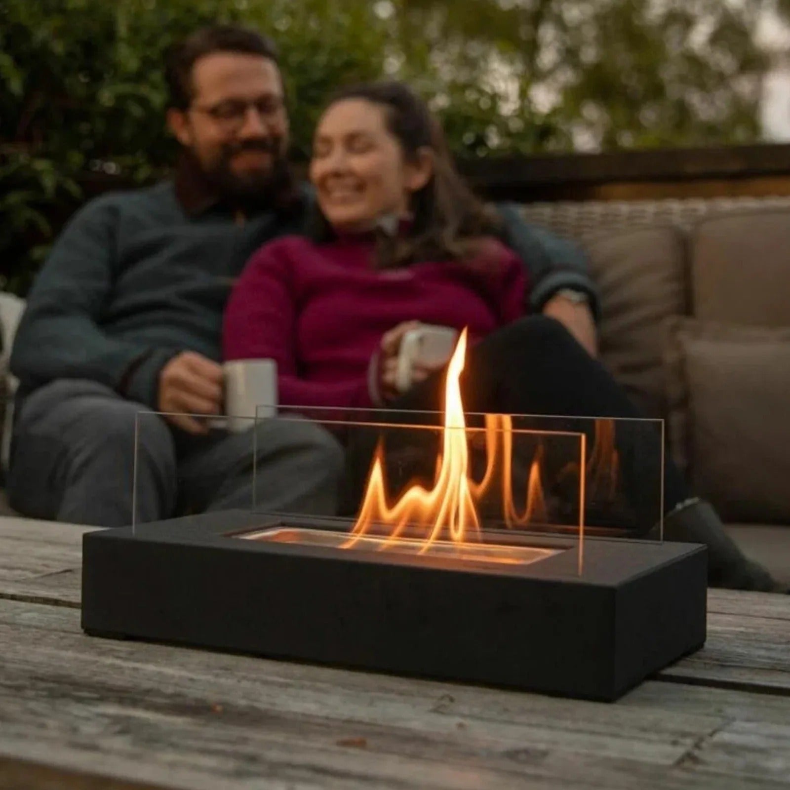 Fitlybuy smokeless black rectangular tabletop bio-ethanol fireplace with clear glass panels, lit on an outdoor table.