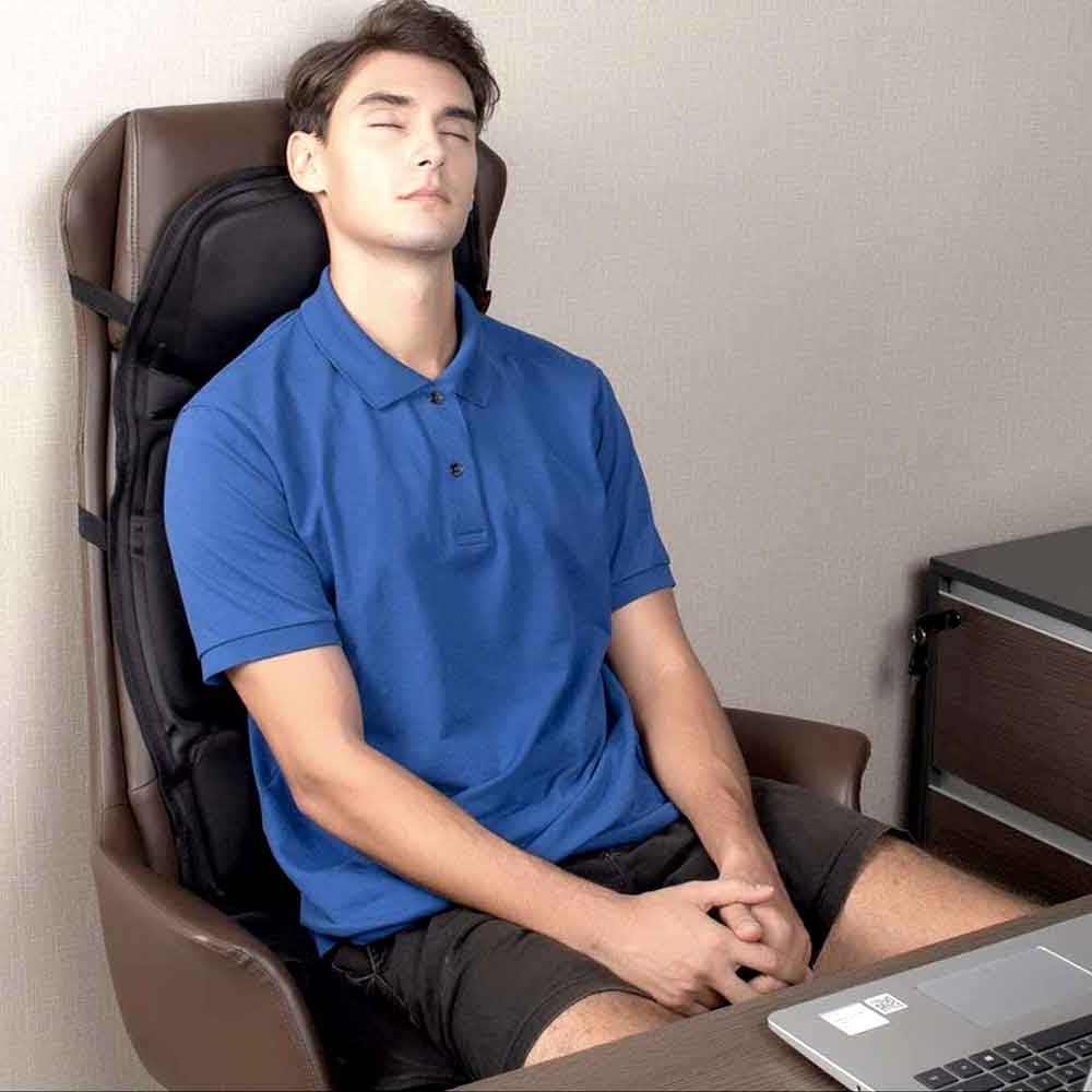 Man wearing blue shirt relaxing in an office chair with a black Fitlybuy 8-mode heated massage pad attached.