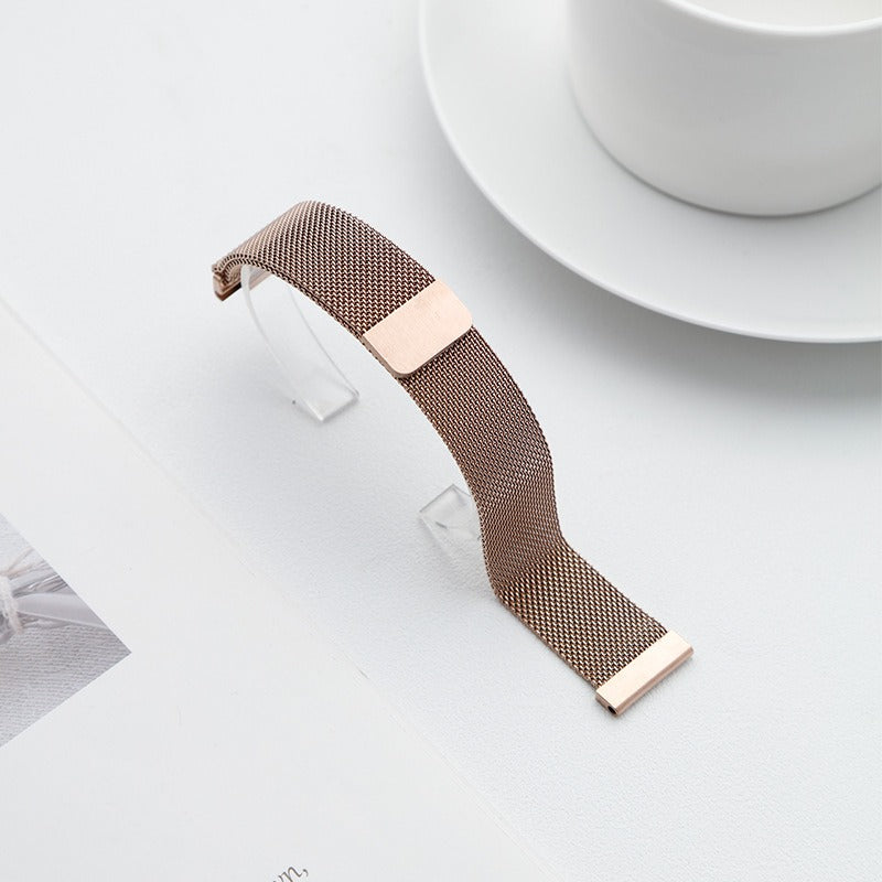 Rose gold Fitlybuy stainless steel Milanese mesh watch strap with adjustable clasp on a white table near a cup.