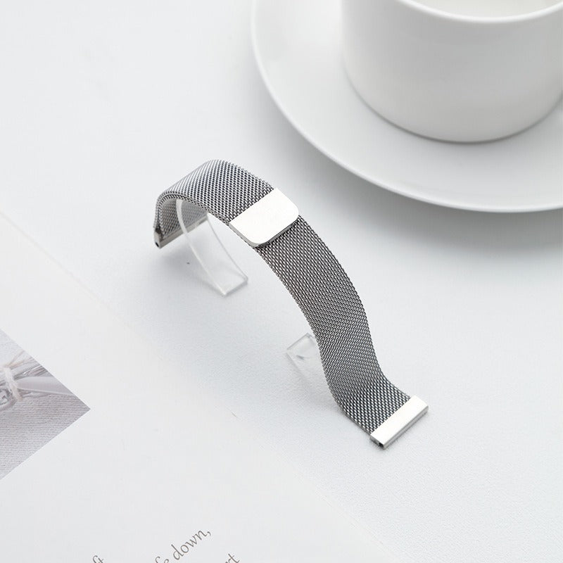 Silver Fitlybuy Milanese stainless steel mesh watch strap with adjustable magnetic clasp on a white table.