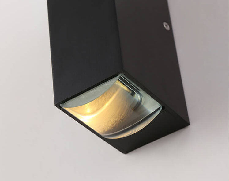 Black rectangular LED outdoor wall light with a clear glass lens glowing with warm light, mounted on a white wall.