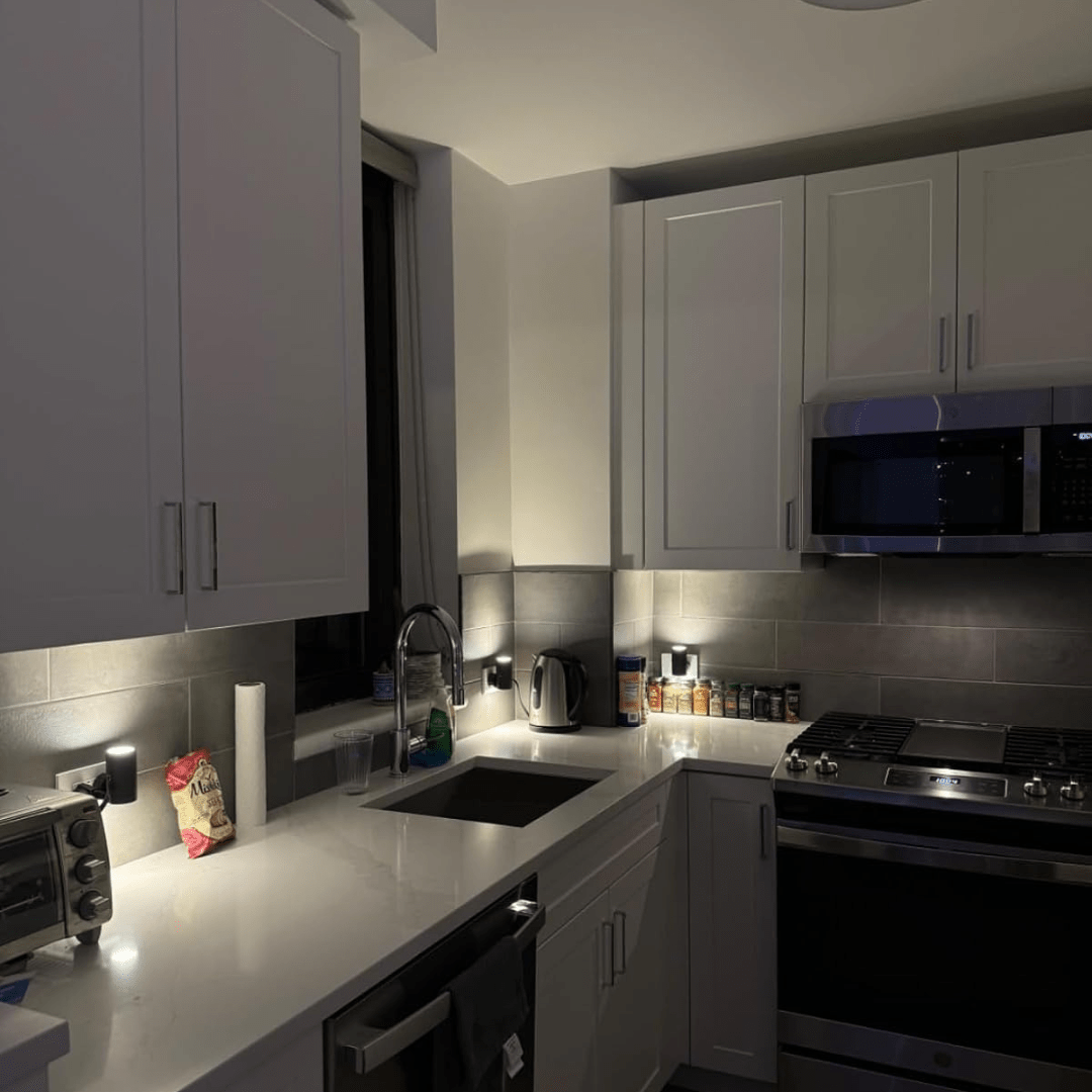Fitlybuy Alova black LED plug-in wall lights illuminate a modern kitchen backsplash, providing soft, dimmable accent light.