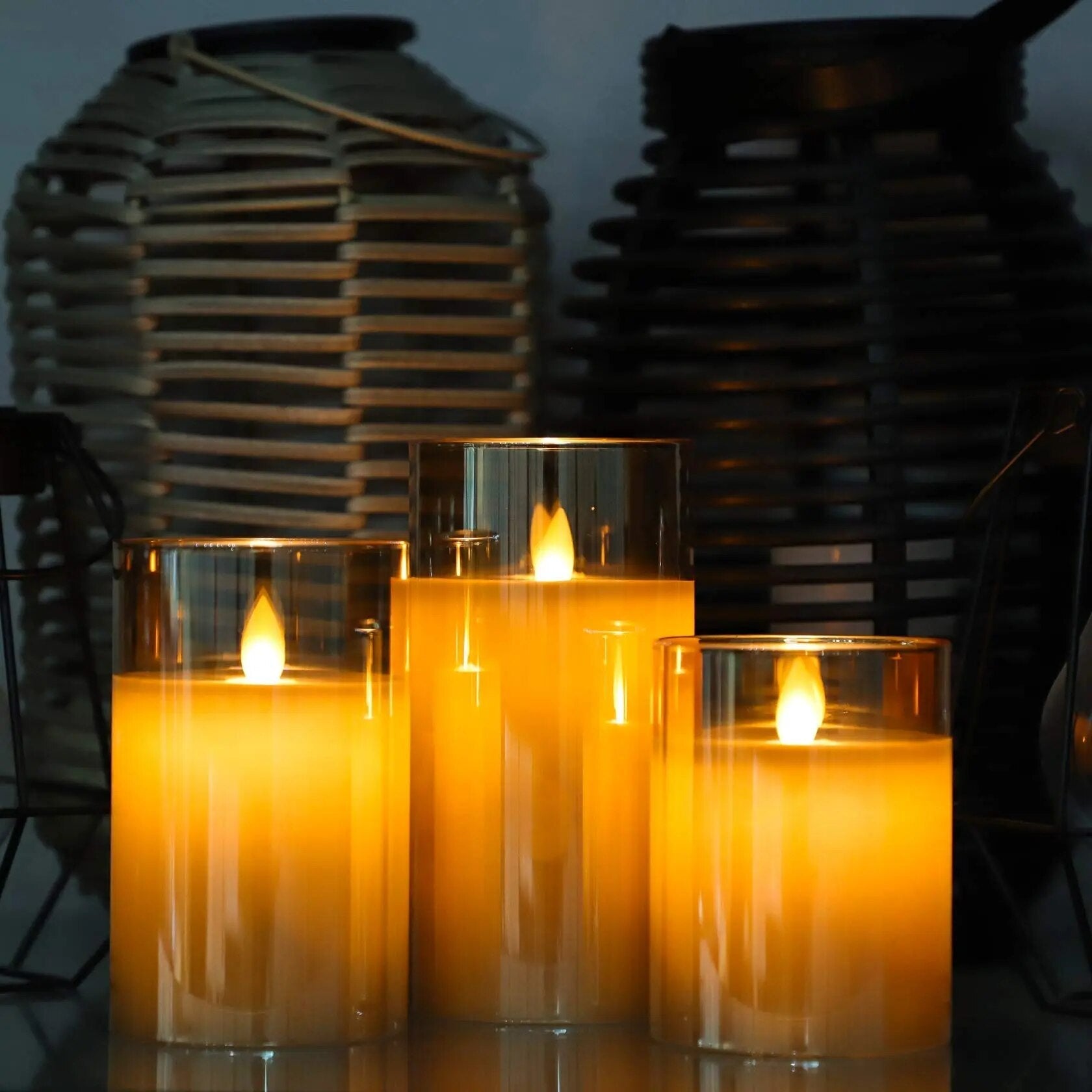 Three Fitlybuy AuraFlame LED candles in glass holders with warm glowing flames, set against decorative lanterns.
