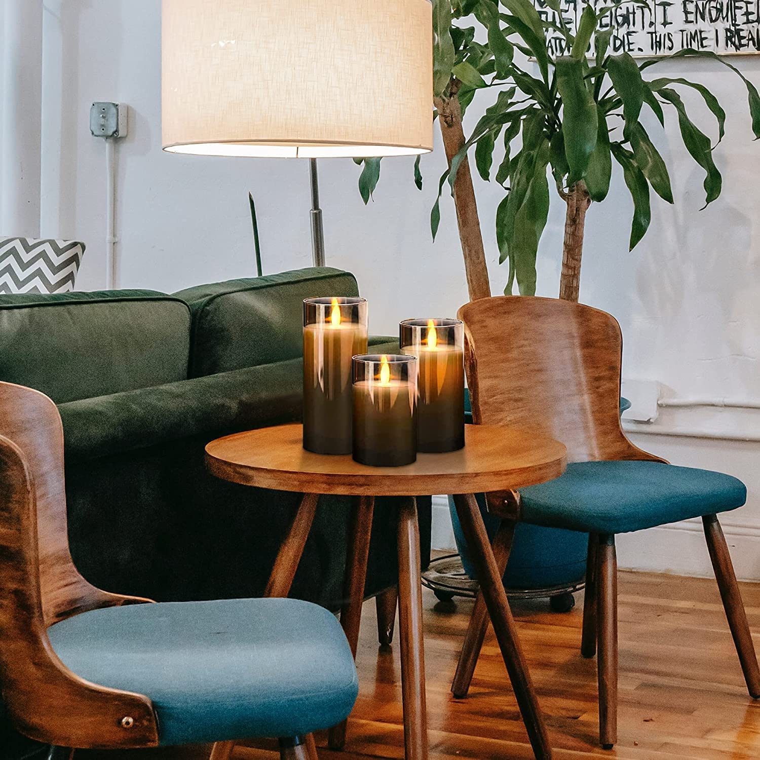 Three Fitlybuy AuraFlame grey flameless LED pillar candles with realistic flickering light on a wooden living room table.