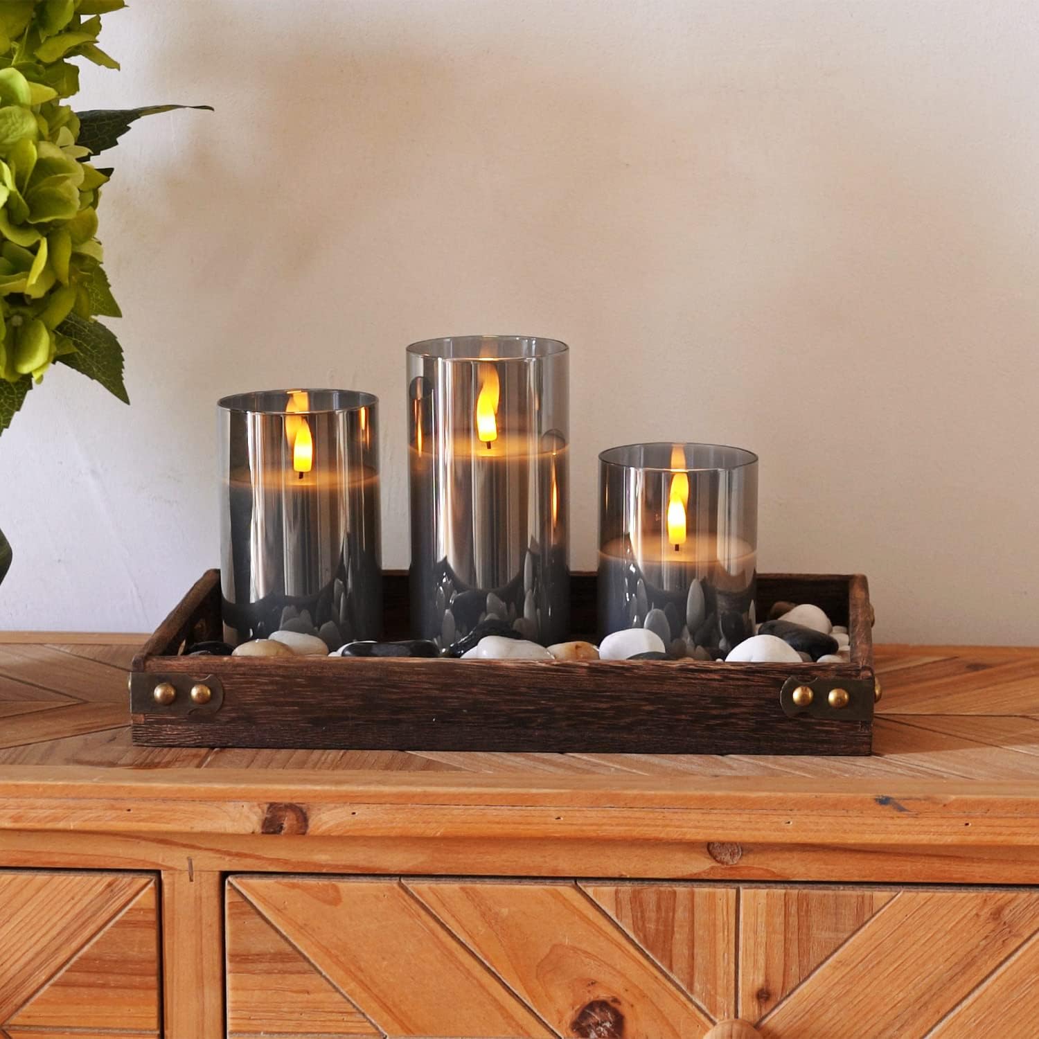 Fitlybuy AuraFlame LED candles in gray glass cylinders on a rustic wooden tray with decorative river stones.