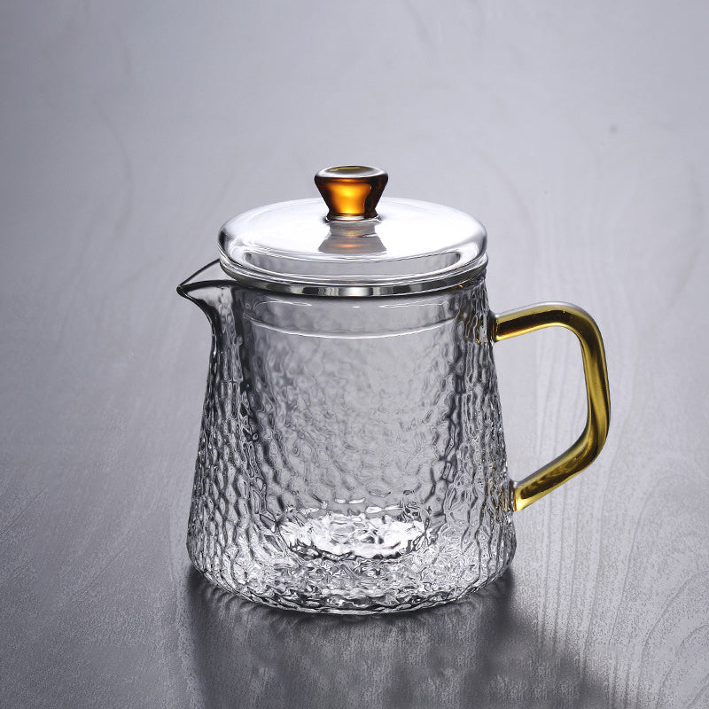 Hammered glass Pindefang teapot with a golden handle and lid knob on a neutral grey background.