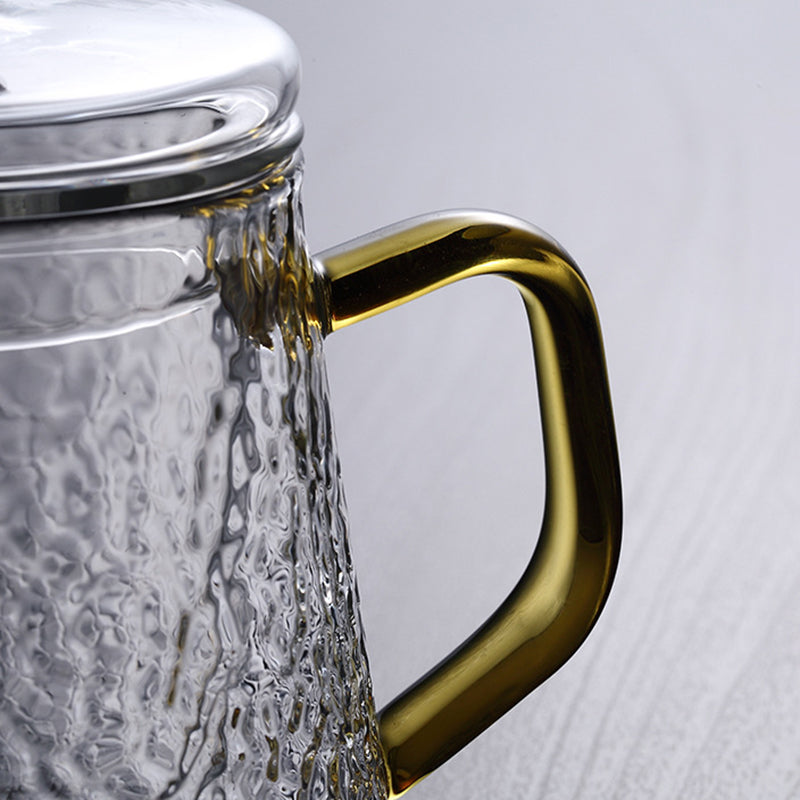Hammered glass teapot with a metallic lid and elegant golden handle, set against a light background.