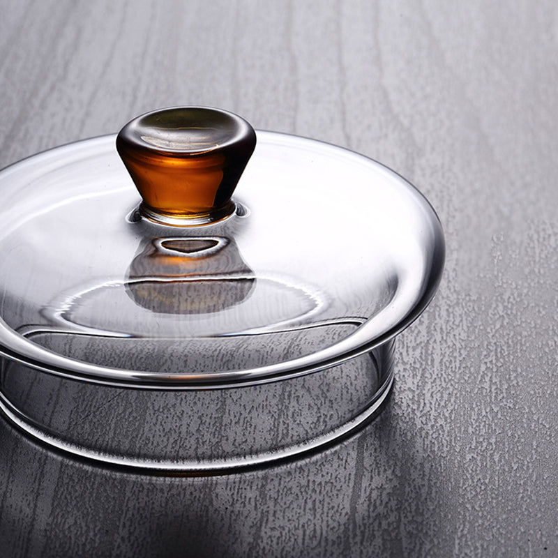 Clear glass lid for Pindefang teapot, featuring a decorative, round amber-colored handle on a gray wooden surface.