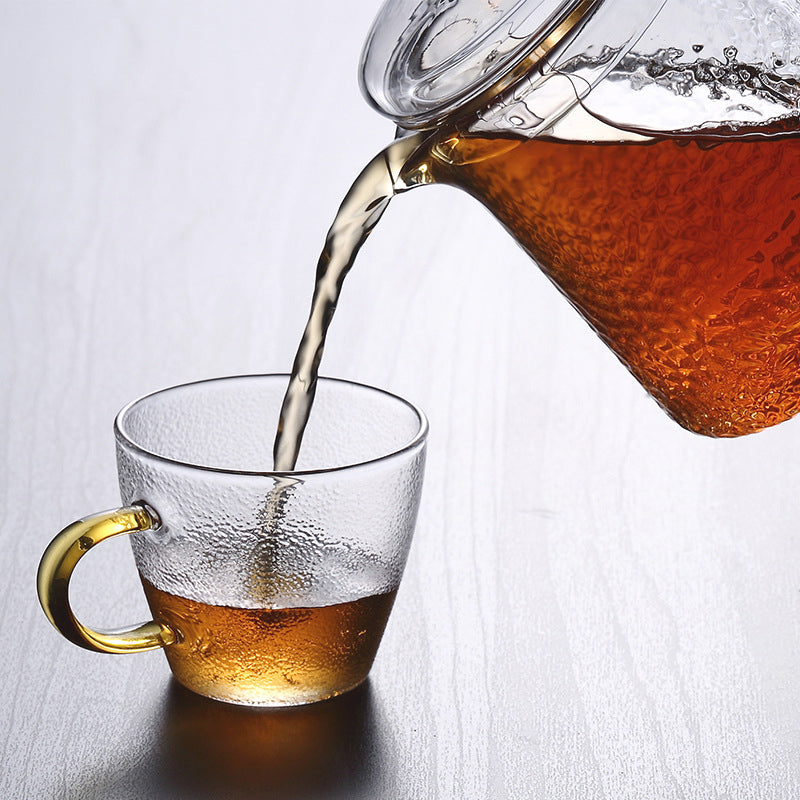 Fitlybuy Pindefang glass teapot with golden handle pouring amber tea into a matching textured glass cup.