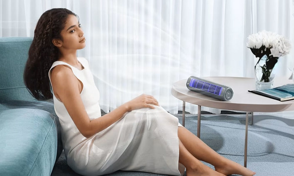 A woman relaxes next to a portable grey Fitlybuy bladeless tower fan with blue light on a coffee table.