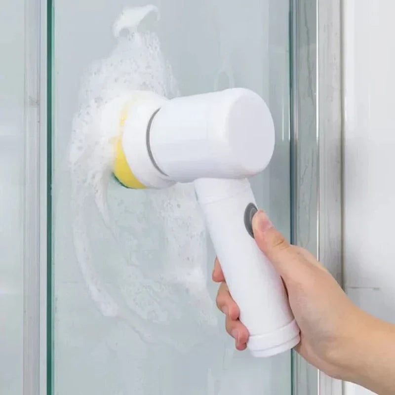 White handheld Fitlybuy electric scrubber with a yellow brush attachment cleaning soap suds off a glass shower door.