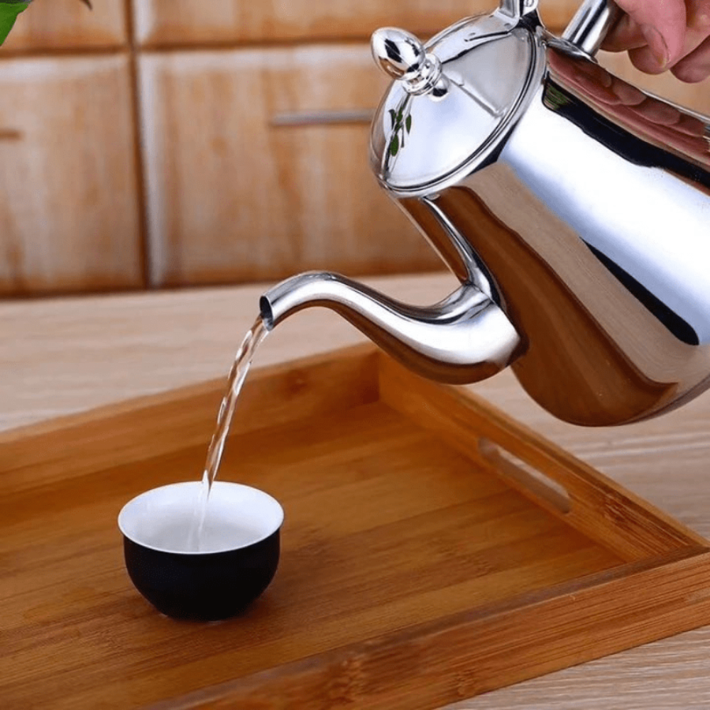 Fitlybuy stainless steel gooseneck kettle pouring water into a small black and white tea cup on a wooden tray.