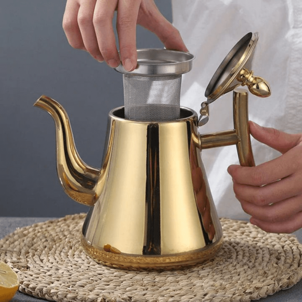 Hands insert a mesh filter into a shiny gold 1.5L Fitlybuy stainless steel induction kettle on a straw mat.