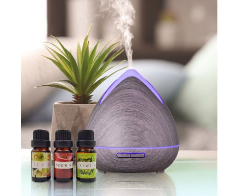 Fitlybuy PureSpa dark wood grain ultrasonic diffuser emitting mist with three essential oil bottles and a plant.