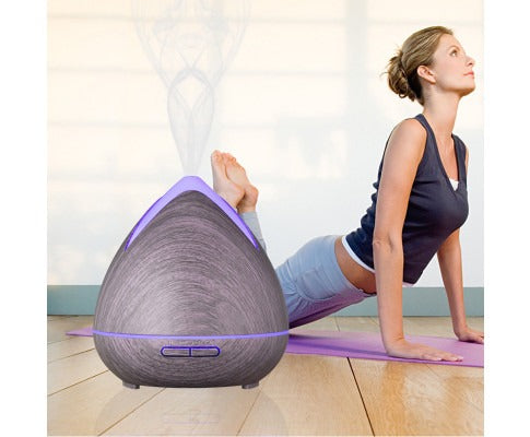 Fitlybuy PureSpa wood-grain ultrasonic diffuser emitting cool mist near a woman doing yoga on a purple mat.