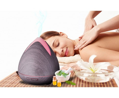 Fitlybuy PureSpa dark wood grain ultrasonic diffuser emitting cool mist next to a woman receiving a spa massage.