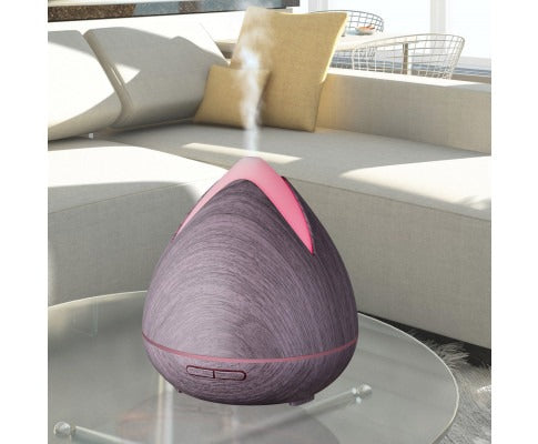Fitlybuy PureSpa ultrasonic diffuser with dark wood grain, glowing pink top, and mist, on a glass table in a living room.
