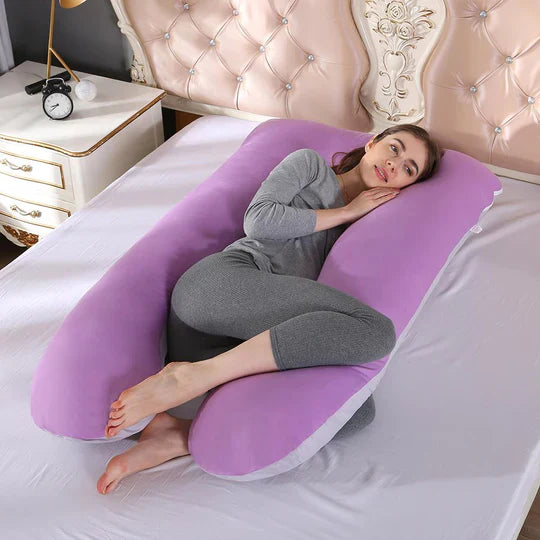 Woman resting on a purple U-shaped Fitlybuy pregnancy full body pillow on a white bed.