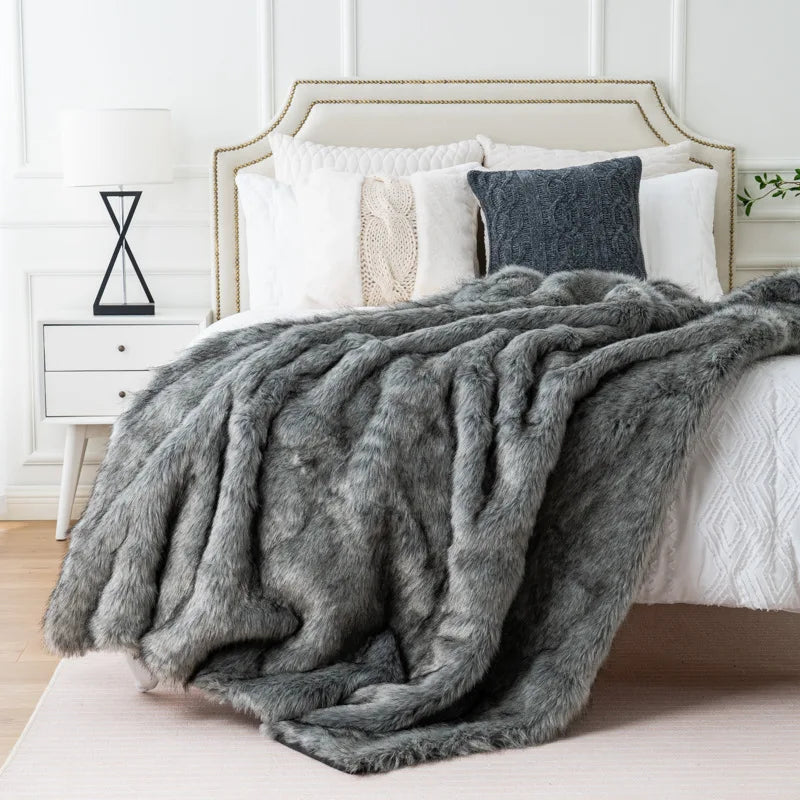 Luxury grey faux fox fur throw blanket draped over a white bed in a modern bedroom setting.