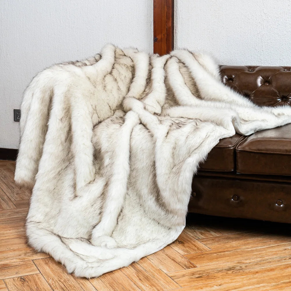 Fitlybuy white and grey faux fox fur throw blanket draped over a brown leather tufted couch on a wooden floor.