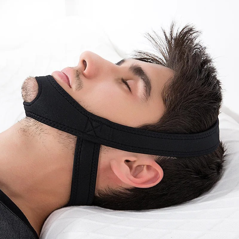 Man sleeping in bed wearing a black, adjustable neoprene Fitlybuy anti-snore chin strap.