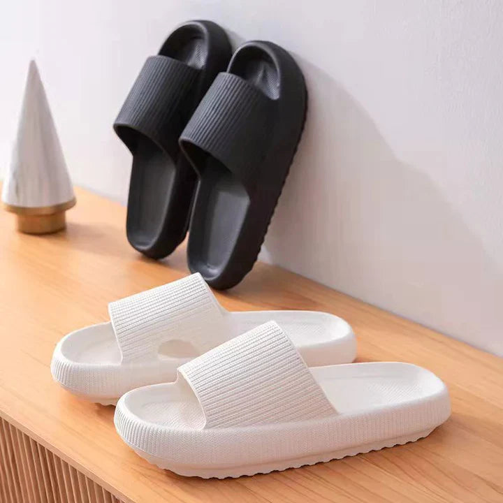Fitlybuy Cloud Slides in black and white with thick, textured ComfortFoam soles, displayed on a wooden surface.