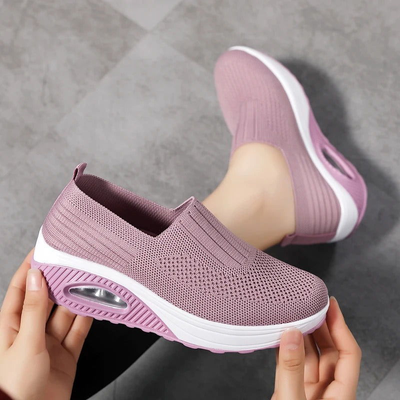 Hands hold a mauve Fitlybuy orthopedic slip-on sneaker with a white cushioned sole and air-sole ComfortGrip tech.