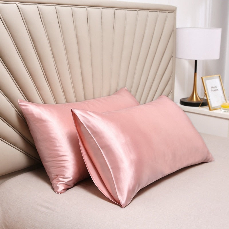Two pink Fitlybuy satin pillowcases with SoftTouch fabric on a bed against a beige upholstered headboard.