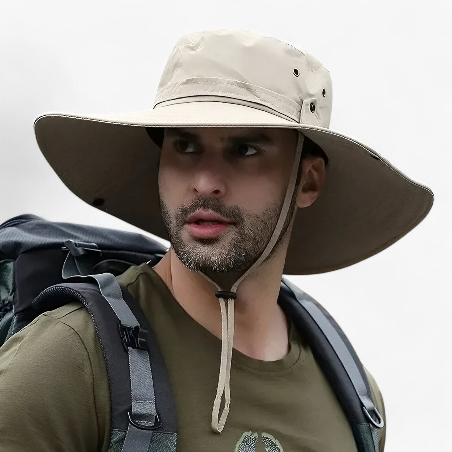 Man wearing a beige Fitlybuy Zeno wide-brim UV protection hat with a chin strap while carrying a hiking backpack.