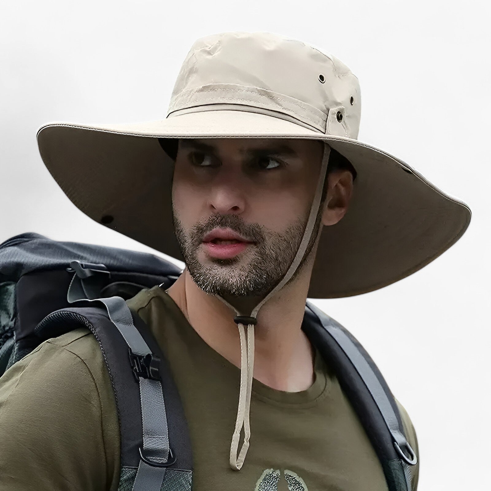 Man wearing a beige Fitlybuy Zeno wide-brim UV protection hat with a chin strap while carrying a hiking backpack.