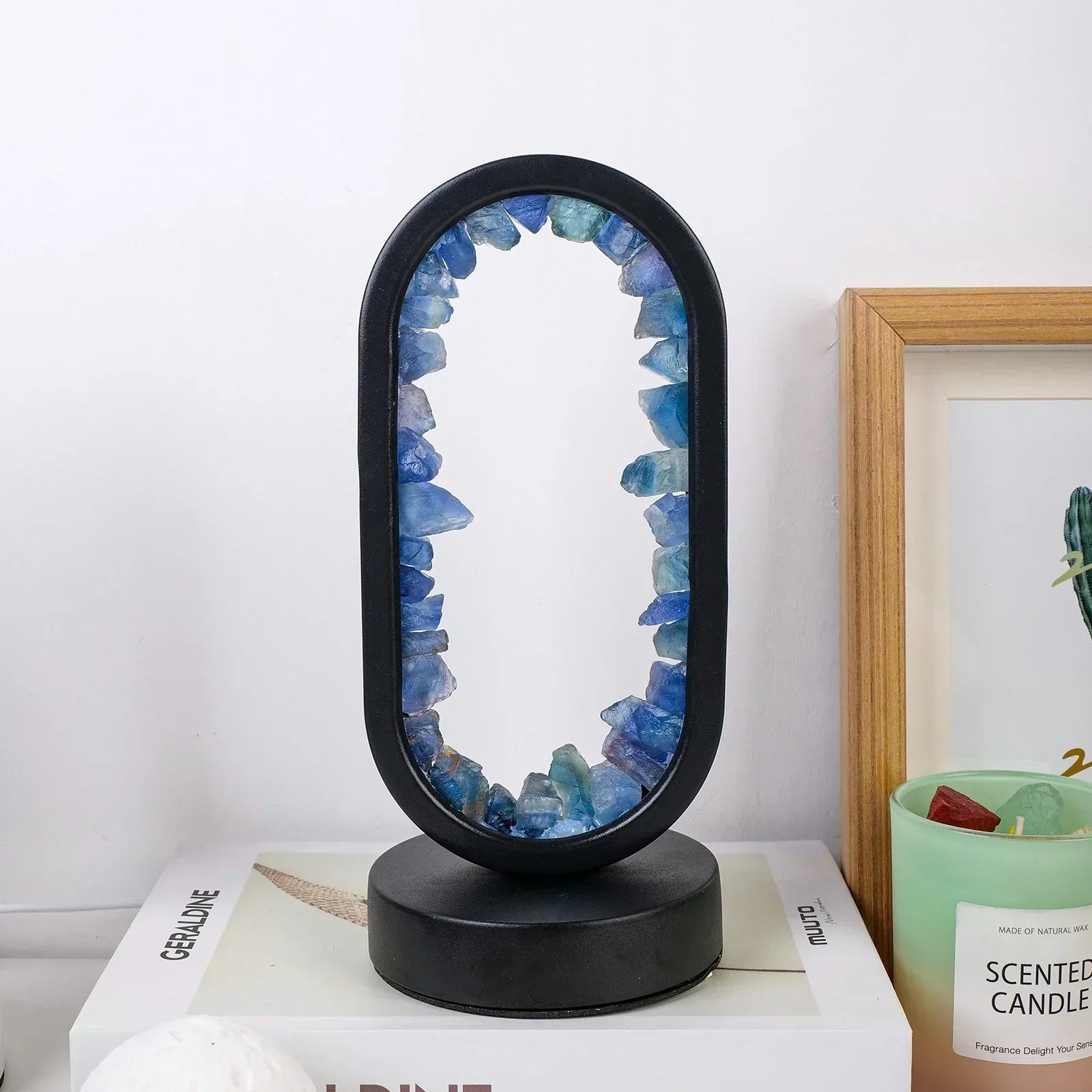 Fitlybuy AuraStone oval lamp with raw blue crystals in a black frame, sitting on a book next to a scented candle.