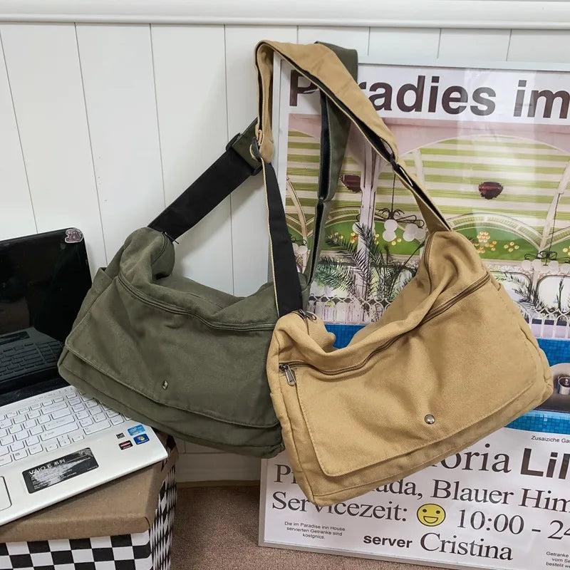 Olive green and tan canvas messenger shoulder bags with zippered pockets and adjustable straps, displayed near a laptop.