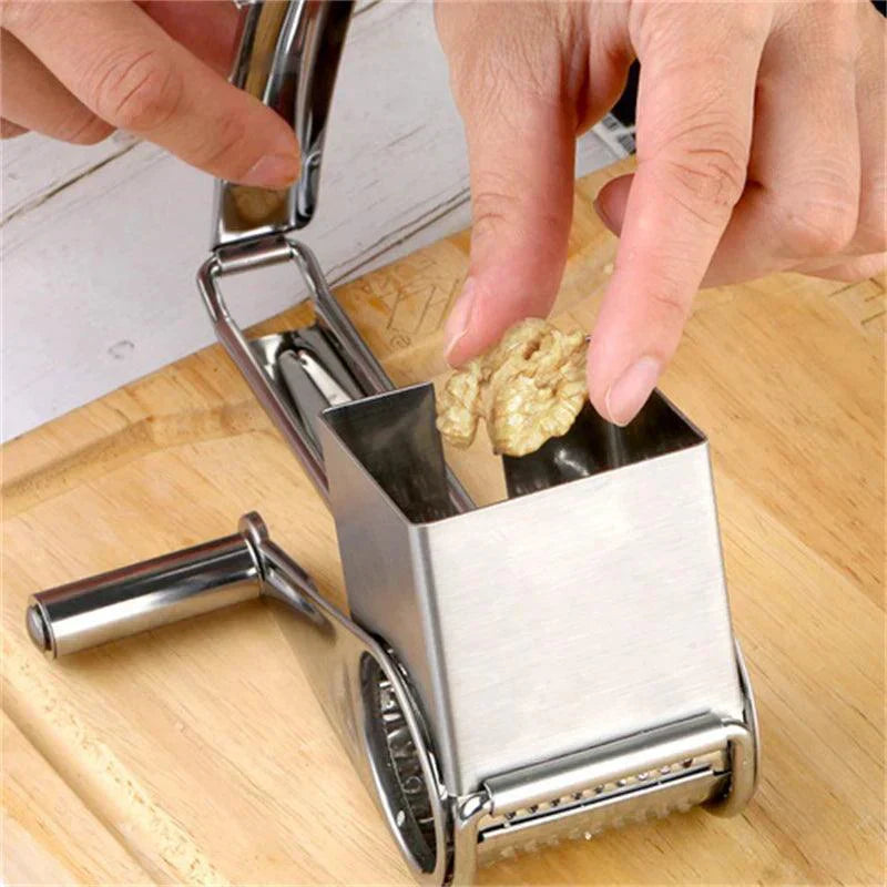 Hands using a silver Fitlybuy stainless steel rotary grater to shred a walnut on a wooden cutting board.
